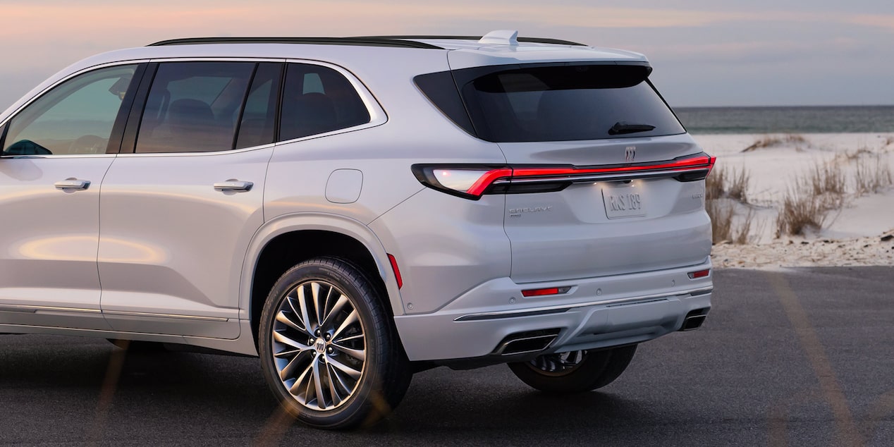 Three-Quarters Rear View of a 2025 White Buick Enclave Parked in Front of a Beach