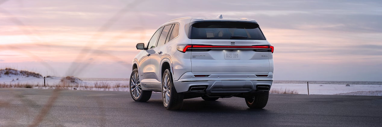 Rear View of a White 2025 Buick Enclave in Front of a Beach Under an Evening Sky