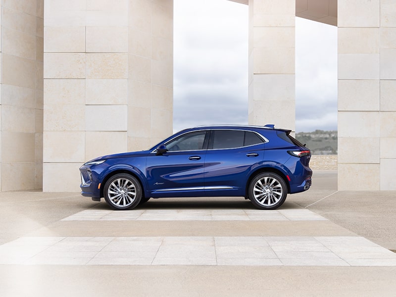 Wide Side View of the 2025 Buick Envision Avenir Luxury SUV Parked Near a Concrete Structure