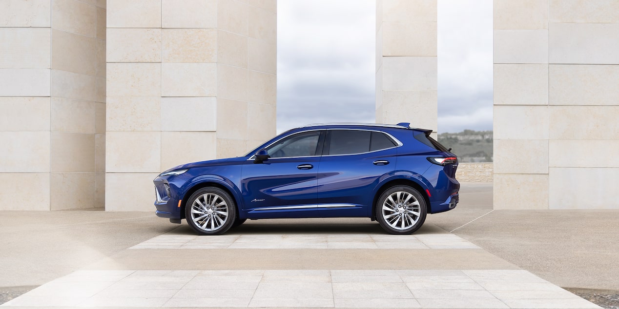 Wide Side View of the 2025 Buick Envision Avenir Luxury SUV Near a Concrete Building