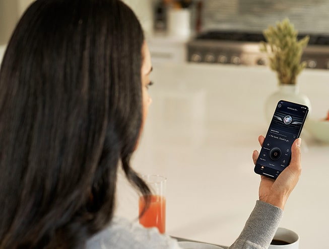 A Woman Sitting in a House Utilizing the MyBuick App on Her Smartphone