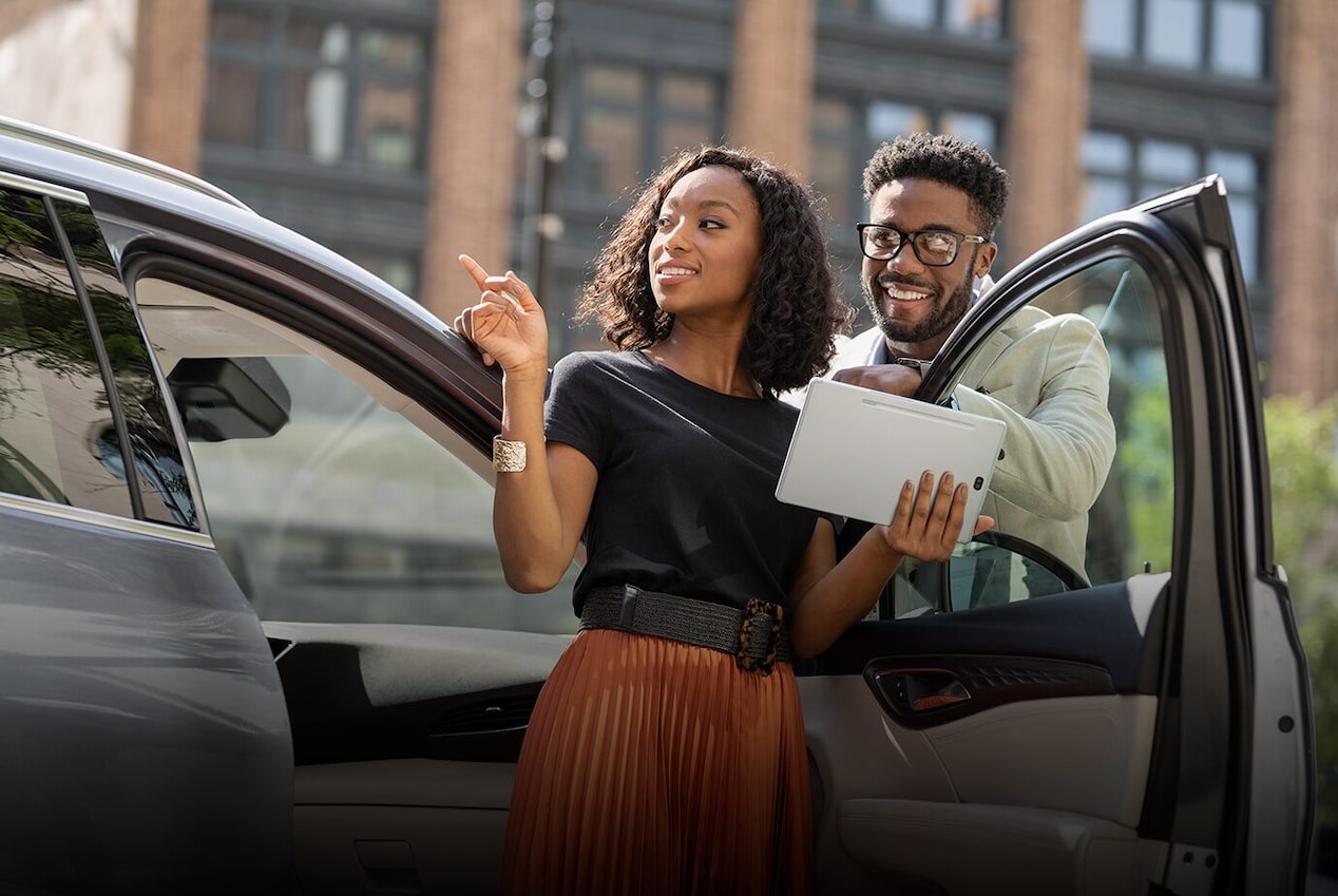 A Couple Smiling While Holding an iPad and Leaning on a Buick Vehicle