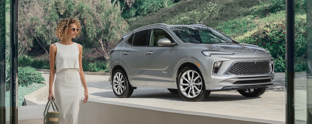 Fashionable Woman Walking From Parked Buick Encore GX Avenir in Driveway