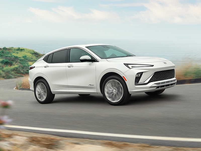 Side Profile View of a White Buick Driving on a Windy Road Next to Coast