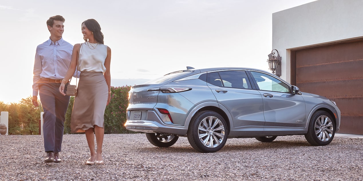 A woman, man and young woman sit inside the living room of a modern home. The all—new Buick Avenir sits in the driveway and is visible from the window