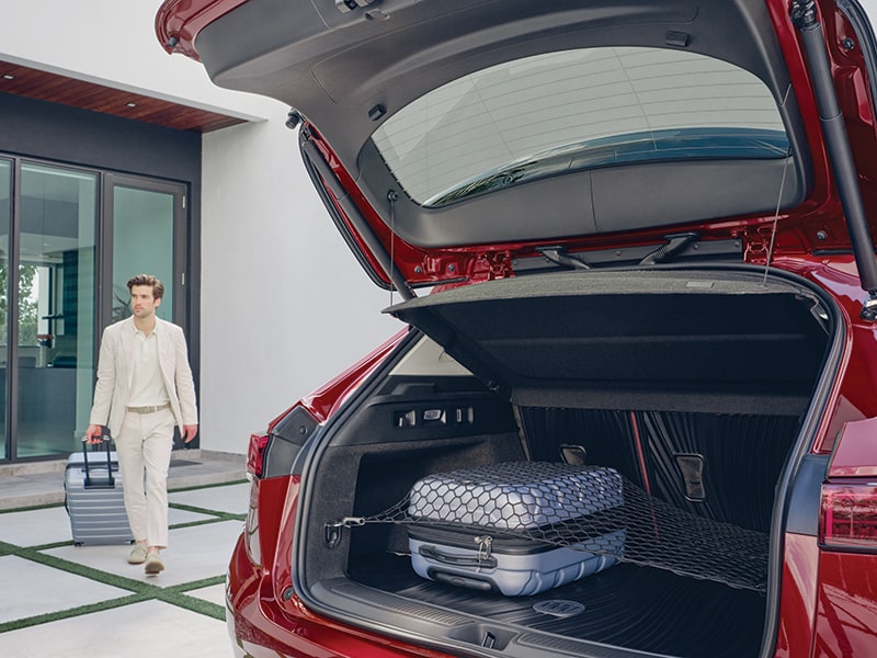 A Man Walking with his Luggage to the Opened Liftgate of a Buick Envision with a Cargo Net and Integrated Cargo Liner Accessory