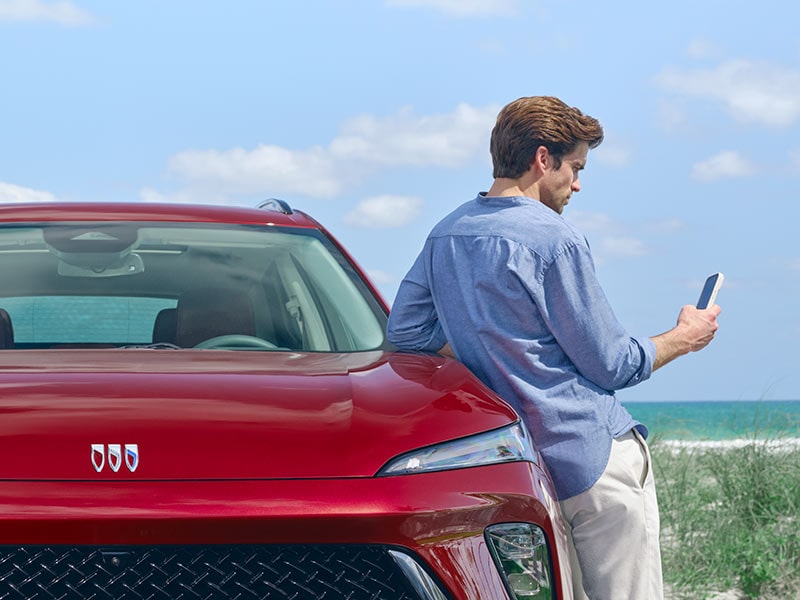 Man on his phone next to a red 2024 Buick Envision